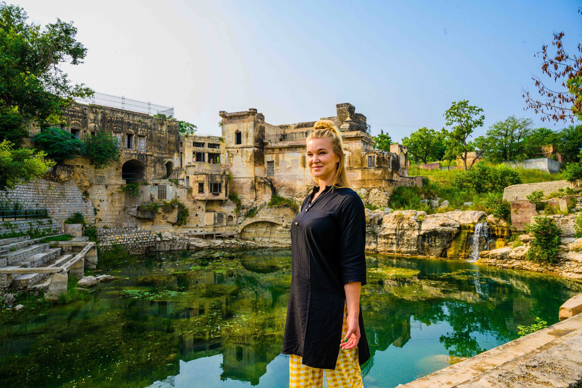 a female tourist visits shri katas raj temple in pakistan. she is standing in front of the sacred pond